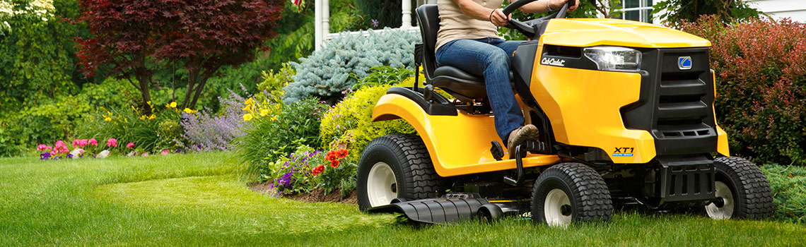 A person on a yellow Cub Cadet® XT1 Enduro mowing a lush front lawn of Kentucky Bluegrass.